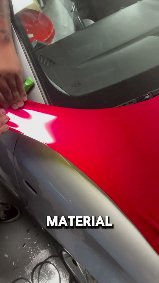 An installer applies heat to an overstretched section of silver vinyl wrap on a car.