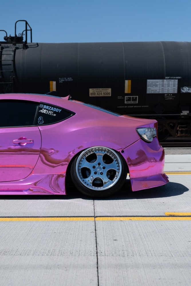 Pink car with chrome rims on a road with a train in the background