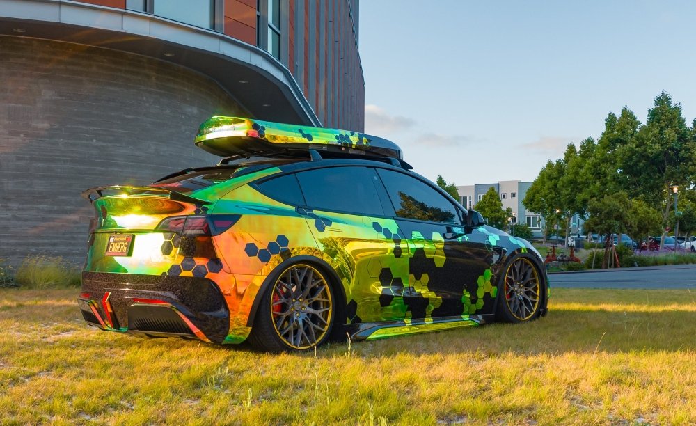Car with a colorful camouflage wrap parked on grass.