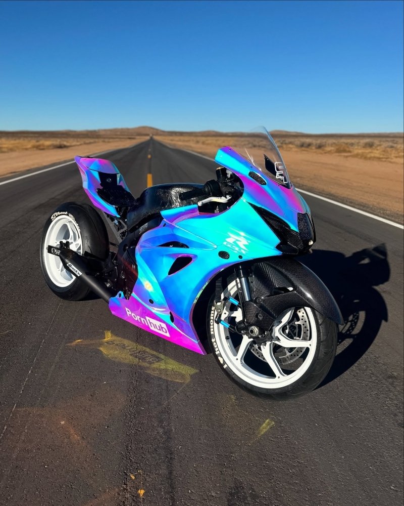 A motorcycle with a blue and purple glossy wrap driving on a road with a desert landscape in the background.