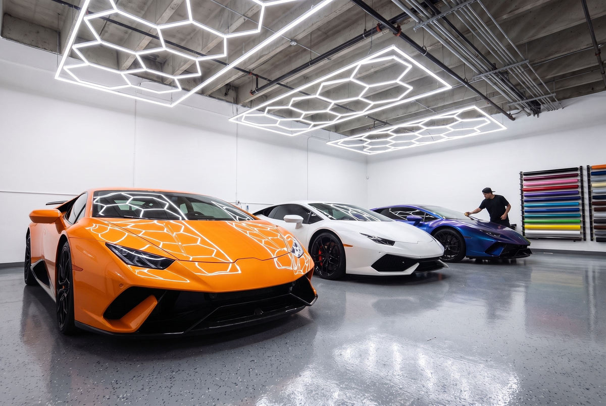 Orange, white and blue-shift supercars under hexagon lights in a wrap shop